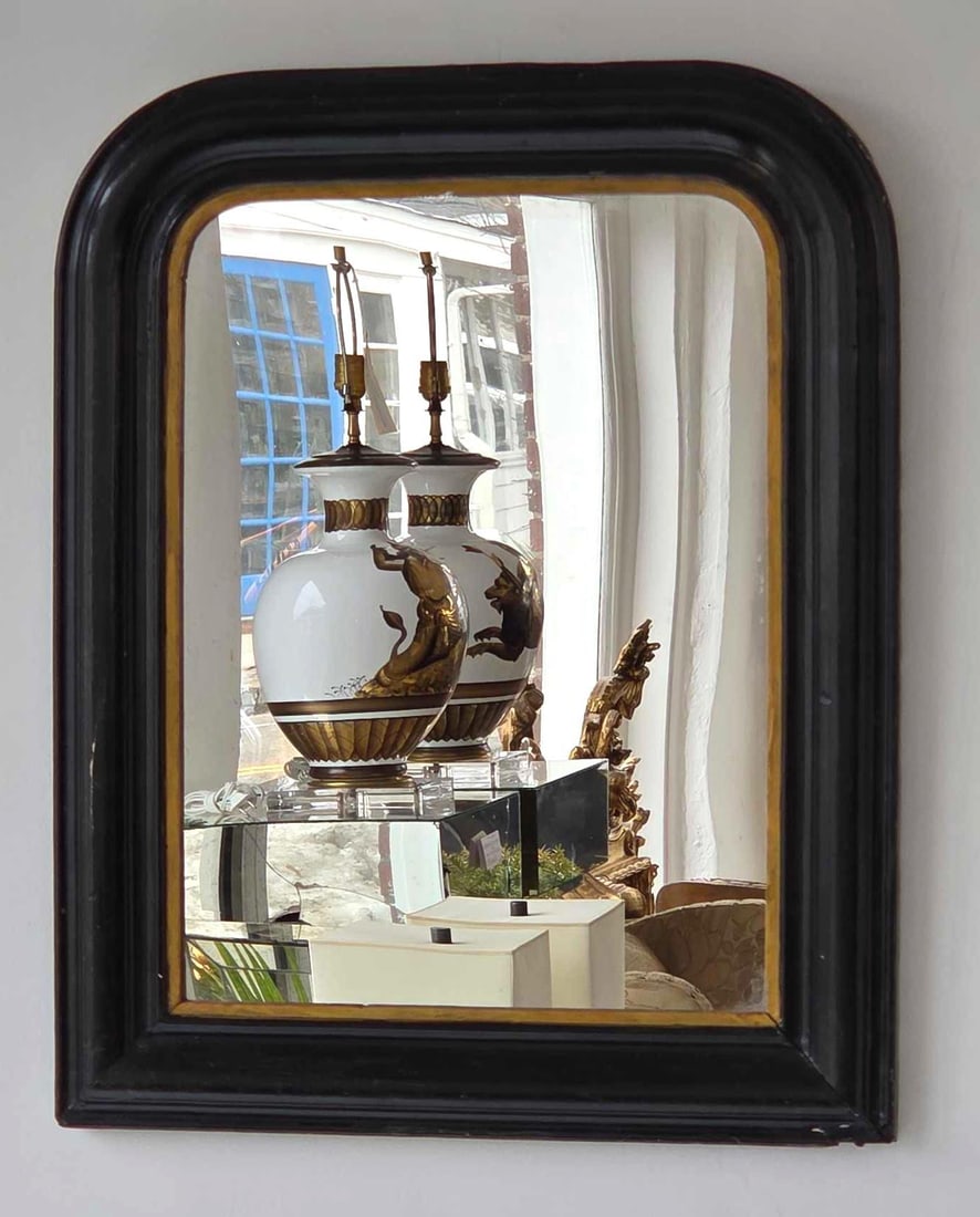 ANTIQUE LOUIS PHILIPPE STYLE BLACK AND GILT FRAMED MIRROR: French-inspired wall mirror with a rounded upper shoulder, ebonized black molded frame, and a thin gilded inner bead. Approximate Dimensions: 24"h x 19.75"w Artist or Maker: Unknown Provena