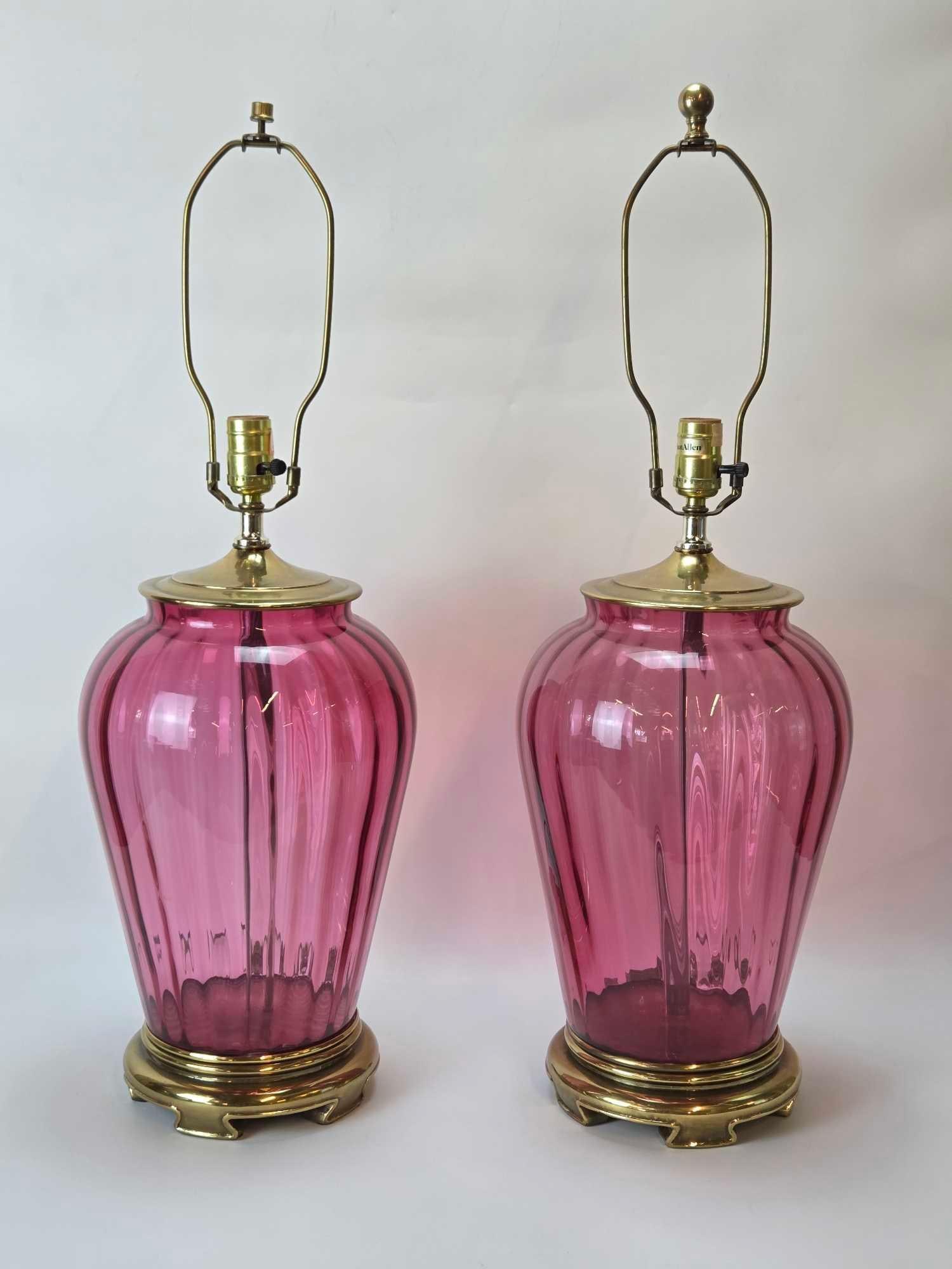 VINTAGE CRANBERRY GLASS BRASS URN TABLE LAMPS PAIR: Ribbed cranberry glass vessels on tiered brass bases with matching metal hardware Approximate Dimensions: 29"h x 9.5"dia Artist or Maker: Unknown Provenance: From a New York