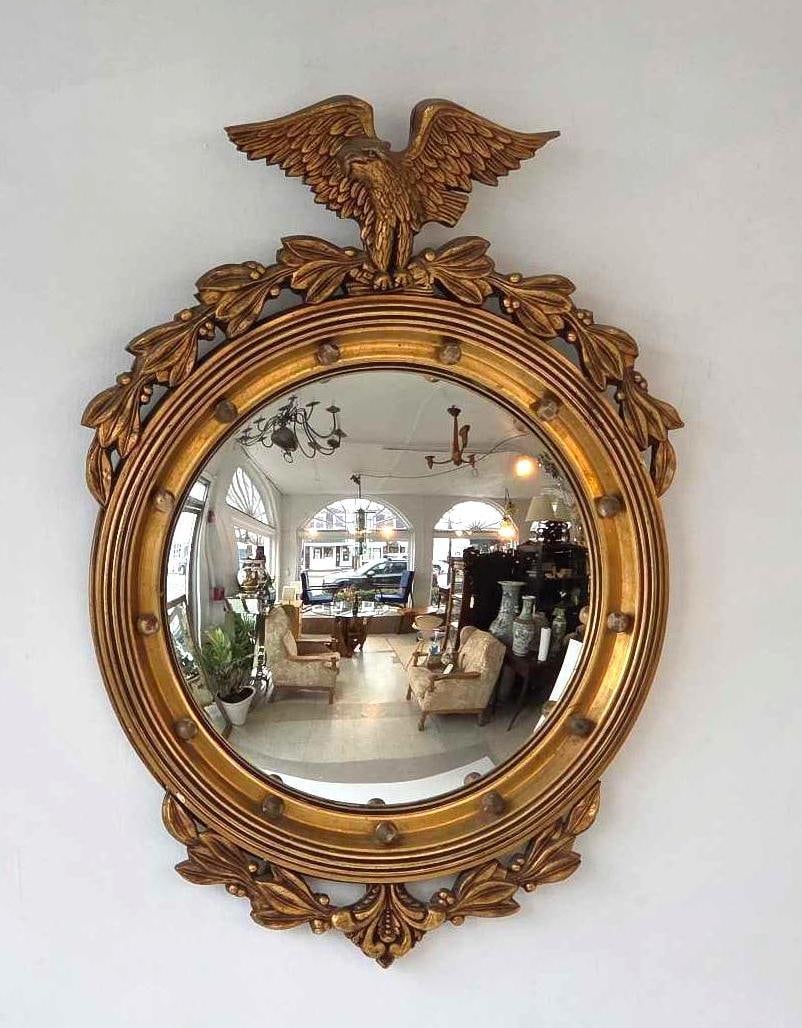 FEDERAL STYLE GILTWOOD EAGLE CONVEX BULLSEYE MIRROR: A circular gilt wood frame mirror with carved spread-wing eagle crest on top. Approximate Dimensions: 30" x 21.25" Artist or Maker: Unknown Provenance: From a New York Collector 