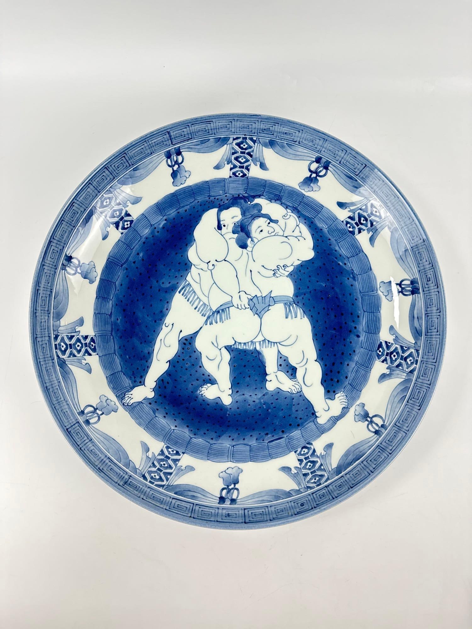 LARGE JAPANESE ARITA STYLE BLUE AND WHITE SUMO WRESTLER CHARGER: Monumental hand-painted porcelain platter featuring a central scene of two Sumo wrestlers in combat surrounded by a geometric border and a six-character mark on the underside. Approximate Dimensions: