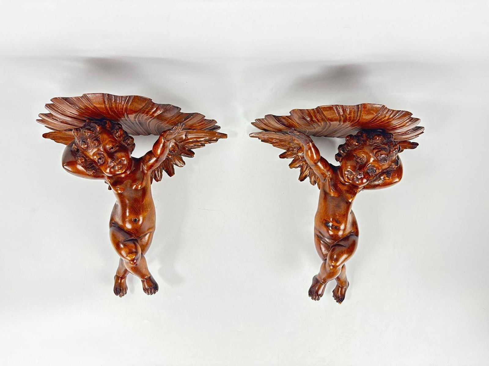 PAIR OF ITALIAN BAROQUE STYLE CARVED WOOD CHERUB WALL BRACKETS: Hand-carved giltwood and polychrome architectural wall corbels in the form of winged putti supporting classical scrolling acanthus leaf platforms. Approximate Dimensions: 15”h x 12.5”w x