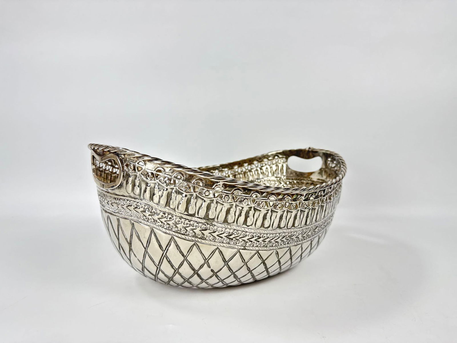 ANTIQUE SHEFFIELD PLATE REPOUSSÉ SILVER ON COPPER BREAD BASKET: Hand-chased oval silver-over-copper serving vessel with a scalloped rim, integrated handles, and a complex diamond-lattice and floral repoussé body. Approximate Dimensions: 7” h x 14”w x