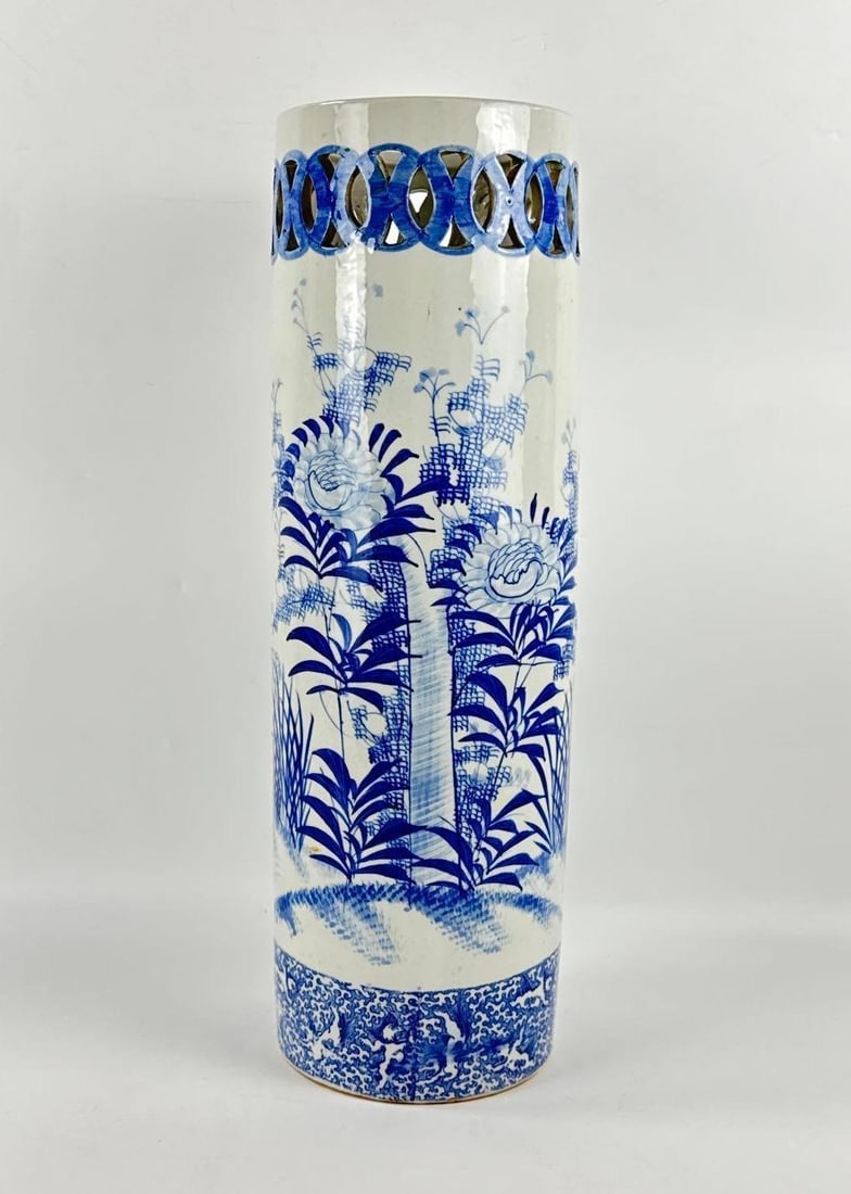 CHINESE BLUE AND WHITE PORCELAIN PIERCED UMBRELLA STAND: Tall cylindrical ceramic vessel decorated with underglaze cobalt blue floral and bamboo landscape motifs with a decorative pierced coin-pattern rim. Approximate Dimensions: 21.5”h x 6.5”w