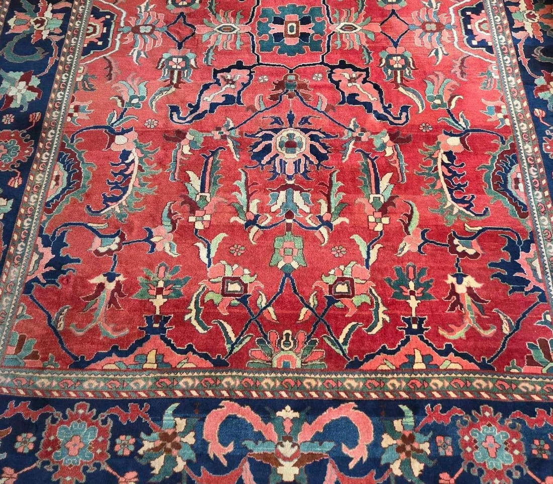 ANTIQUE PERSIAN HERIZ SERAPI ROOM SIZE RUG: A hand-knotted wool carpet featuring a geometric central medallion, a wide stylized floral border, and white fringe on the edges. Approximate Dimensions: 10'-5" x 14'-2" Artist or Ma