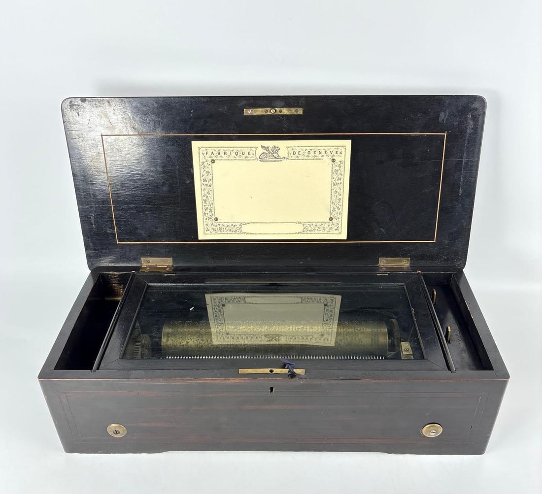 ANTIQUE SWISS CYLINDER MUSIC BOX FABRIQUE DE GENEVE: *Large 19th-century Swiss cylinder music box in ebonized wood case with internal glass dust cover. Approximate Dimensions: 5.25"h x 20"w x 9"d Artist or Maker: Fabrique de Geneve