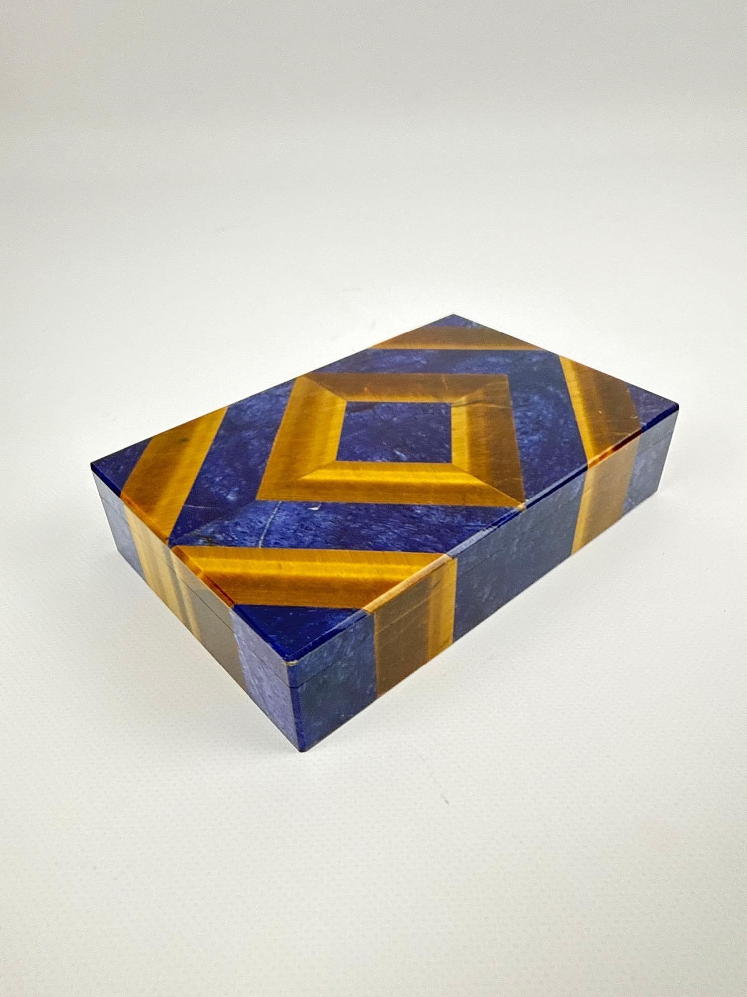 ROMANELLI ITALIAN PIETRA DURA LAPIS LAZULI AND TIGER'S EYE BOX: Rectangular specimen stone trinket box with geometric inlaid lid and marble base Approximate Dimensions: 1.75”h x 5.25”w x 3.5”d Artist or Maker: Romanelli Pro