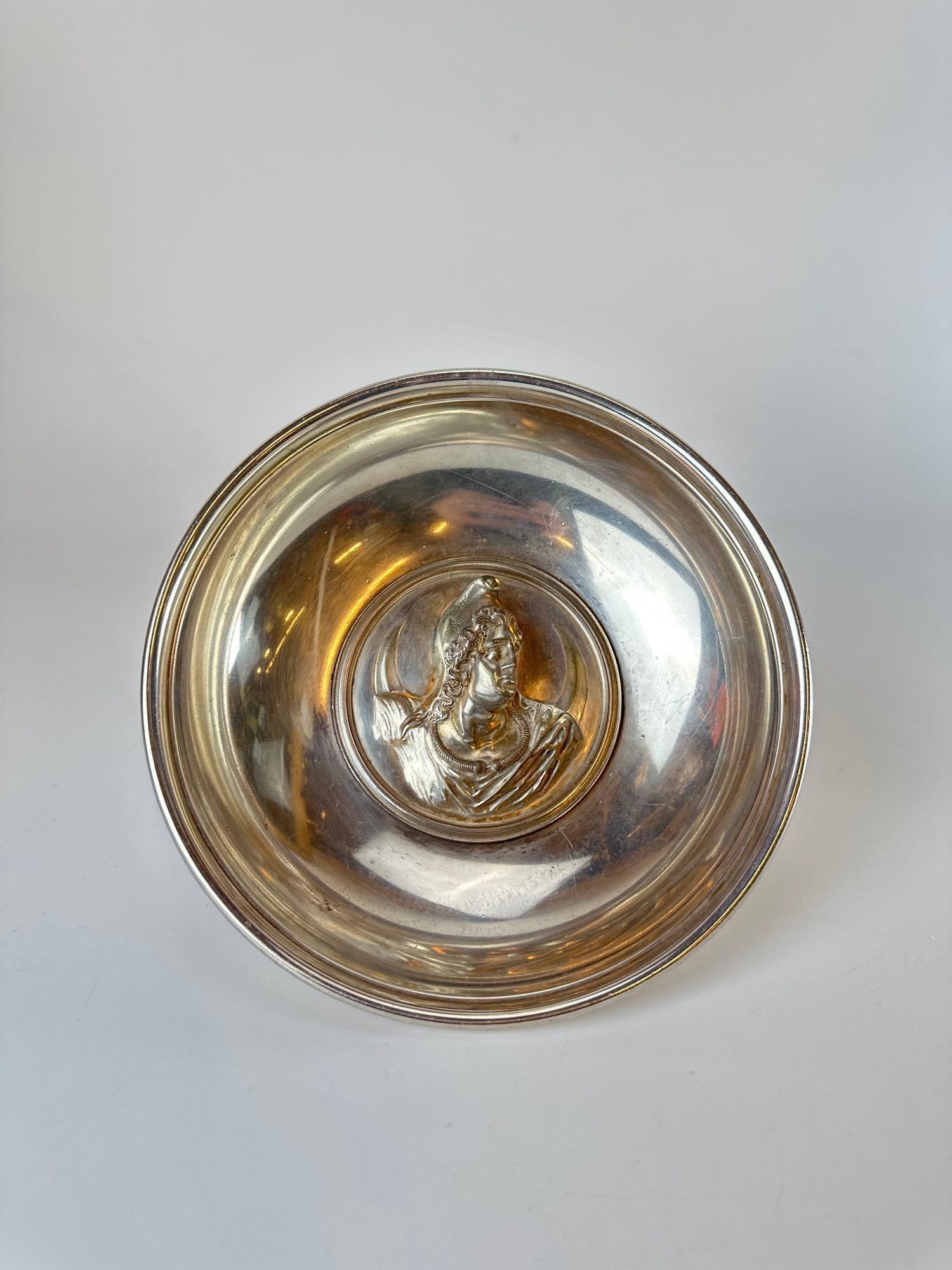 SILVER-PLATE NEOCLASSICAL PATERA DISH DEPICTING ATTIS: A decorative silver-plated libation or "patera" dish featuring a central high-relief (repoussé) medallion. Approximate Dimensions: 2"H x 7.75"Dia Artist or Maker: Unknown