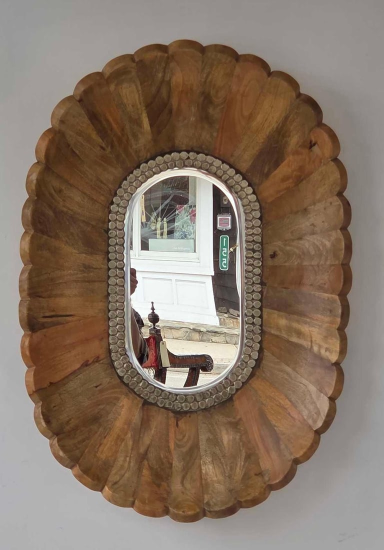 BOHEMIAN SCALLOPED CARVED WOOD WALL MIRROR: Large oval wall mirror with a deep scalloped sunburst-carved wood frame and an inner border of decorative embossed metal medallions Approximate Dimensions: 36.25"h x 25"w x 4"d Artist or M