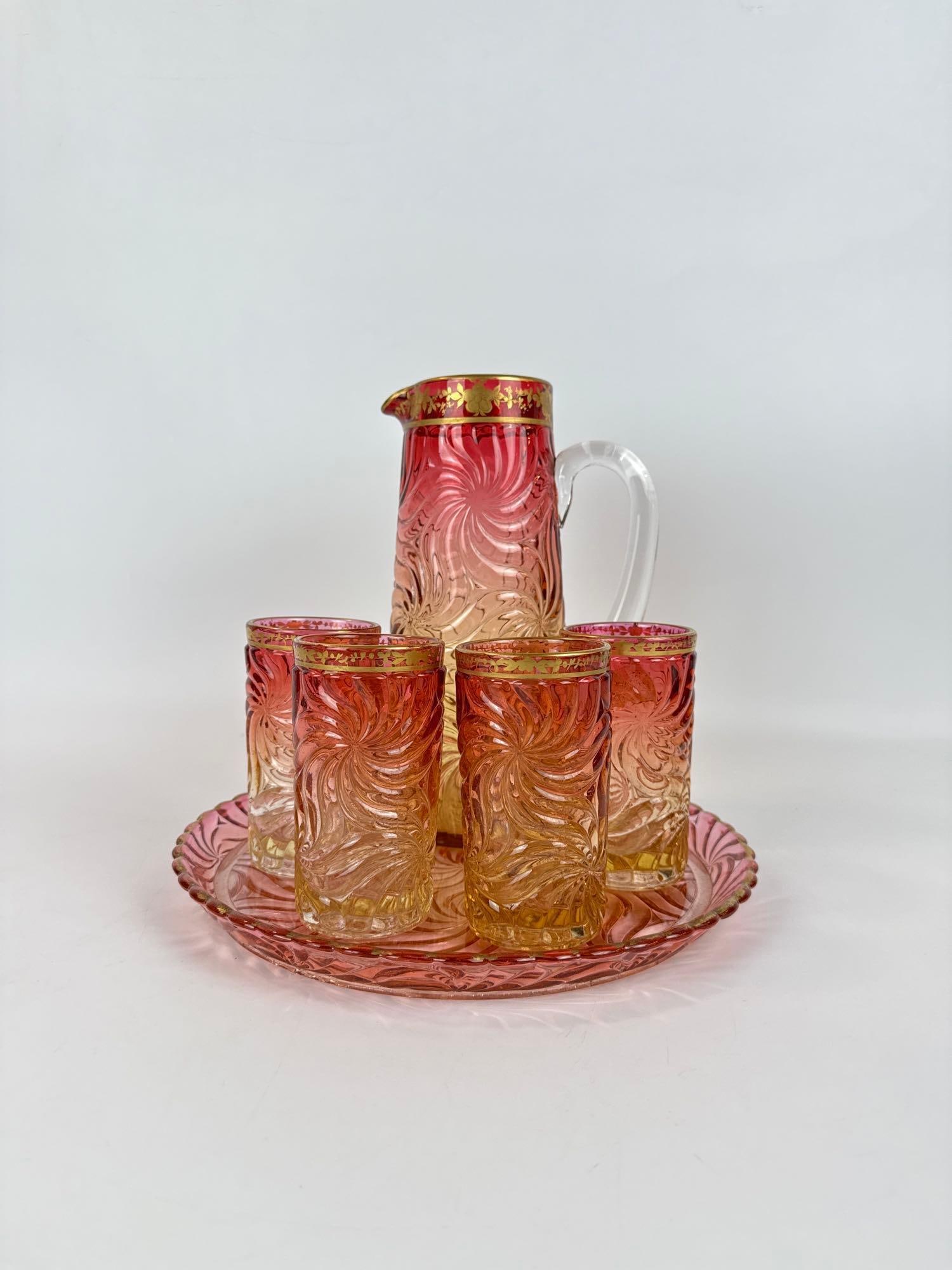 BACCARAT FRANCE CRYSTAL AMBERINA SWIRL PITCHER and TUMBLER SET: *Rare six-piece signed Baccarat molded glass beverage set in amberina ombré with gold gilt rims and pinwheel swirl pattern on matching round tray. Approximate Dimensions: Pitcher 10”h x7.25&rdq