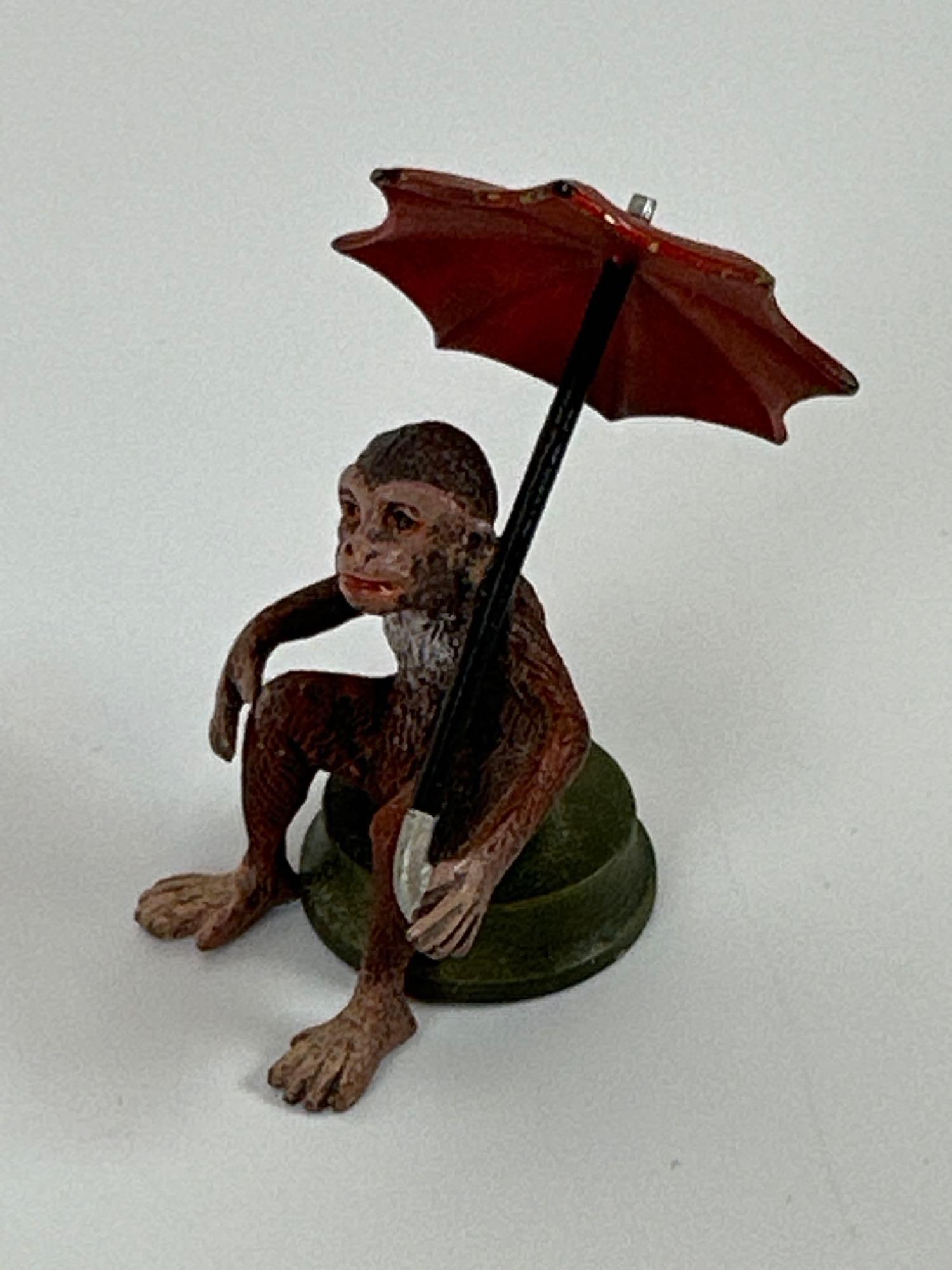 MINIATURE ANTIQUE STYLE COLD-PAINTED BRONZE MONKEY WITH UMBRELLA: *Small-scale miniature figurine in the Vienna Bronze tradition, featuring a seated monkey holding a vibrant red umbrella. This piece is "cold-painted," a technique involving multiple layers of enamel 