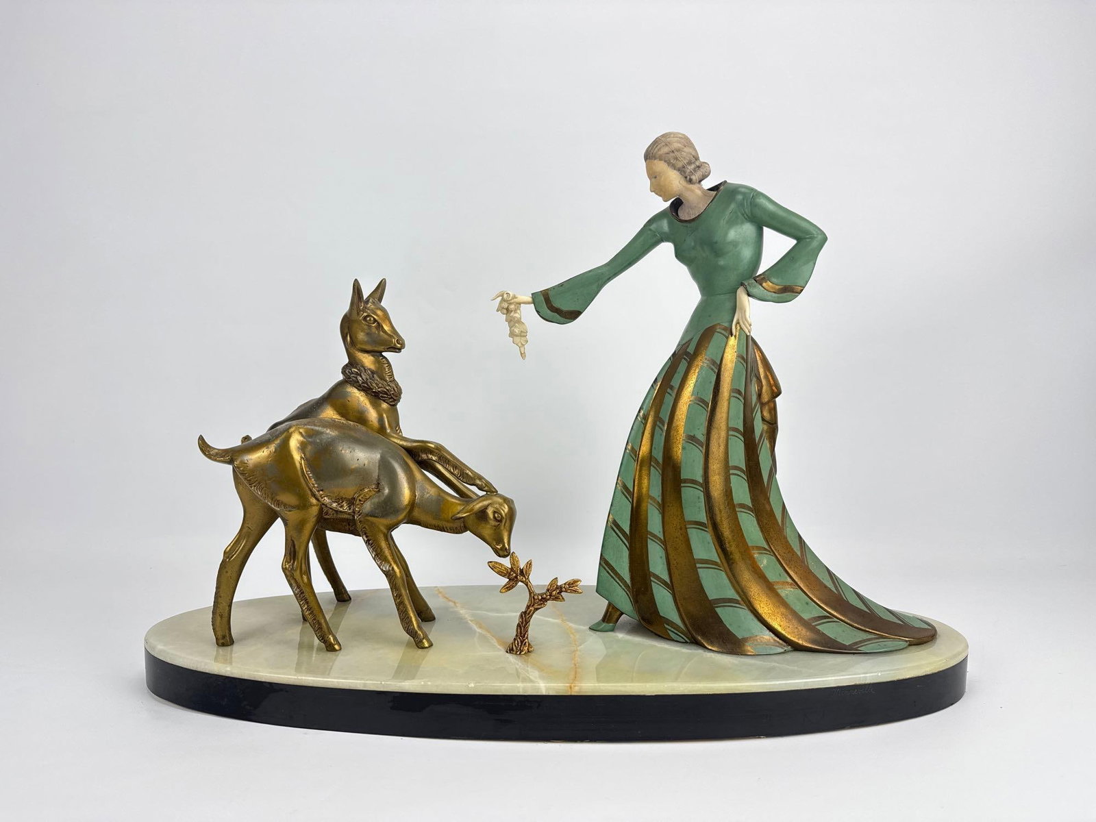 MENNEVILLE-STYLE ART DECO FEMALE WITH FAUNS SCULPTURE: Stylized cold-painted metal figure of a woman in flowing green gown feeding two young deer on an oval multi-colored onyx and black marble base. Approximate Dimensions: 14.5”h x 24”w x 8&rd