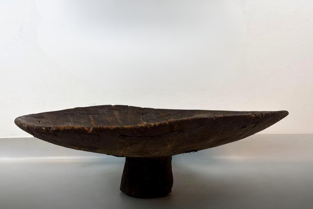 MASSIVE ANTIQUE MOROCCAN BERBER HAND-CARVED WOODEN TAZZABERBER TAZZA (3 OF 3): Large-scale rustic tribal offering bowl or low table carved from a single piece of hardwood with a pedestal base and iron ring handles. Approximate Dimensions: 14” h x 36” dia Artist<