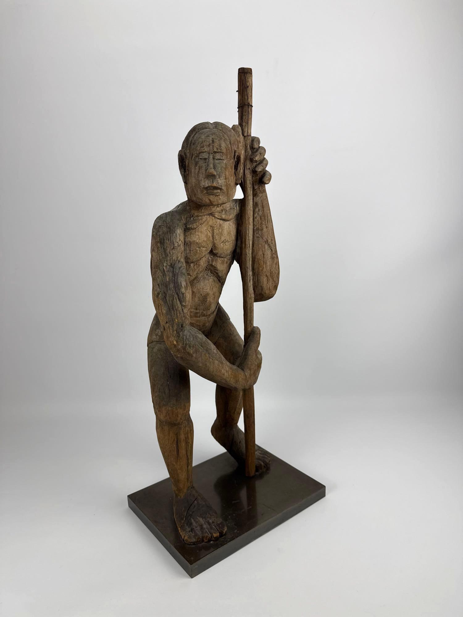 SOUTHEAST ASIAN CARVED IRONWOOD TRIBAL WARRIOR FIGURE: *Hand-carved primitive hardwood sculpture of a crouched male figure holding a staff on a custom gallery mount Approximate Dimensions: 10” x 8” x 26” T Artist or Maker: Unknown <