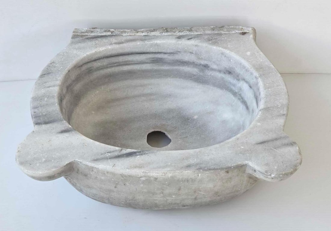 ANTIQUE CARRARA MARBLE SINK BASIN: Hand-carved white and grey veined marble basin with a rounded oval interior and three decorative mounting or support lugs. Approximate Dimensions: 6.75"h x 18.75"w x 16"d Artist or Maker: 