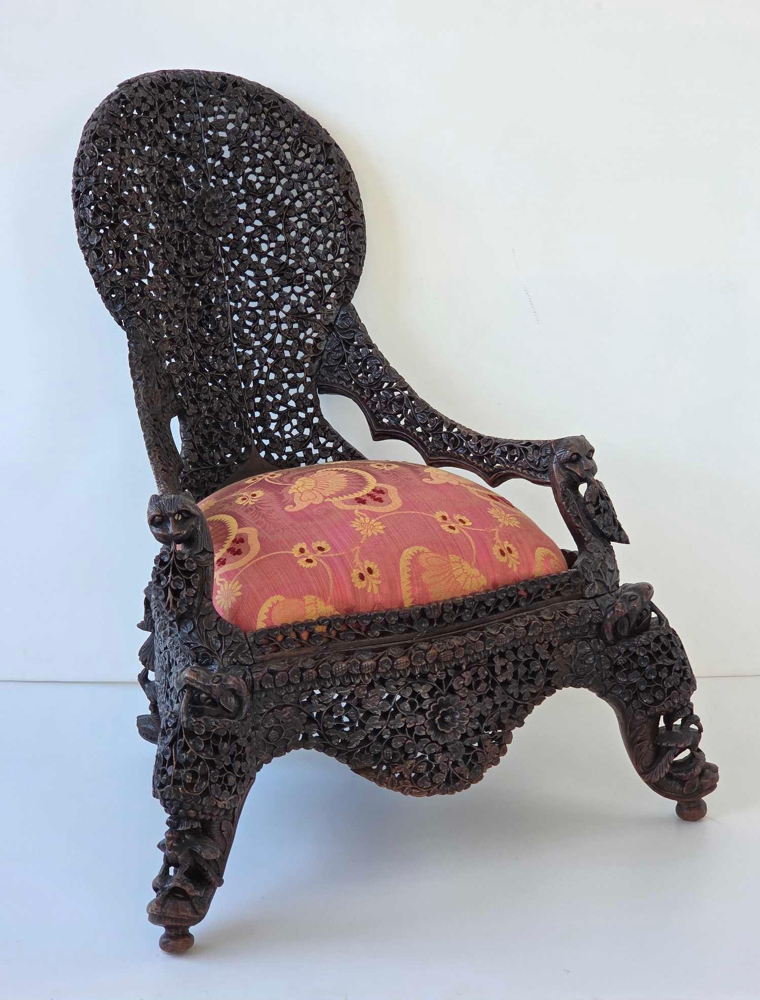 RARE ANGLO INDIAN RAJ DIMINUTIVE CHAIR CIRCA 1890: An ornately hand-carved armchair featuring dense pierced fretwork with foliate and animal motifs and upholstered seat cushion. Approximate Dimensions: 31"H x 27.25"W x 27"D Artist or Maker