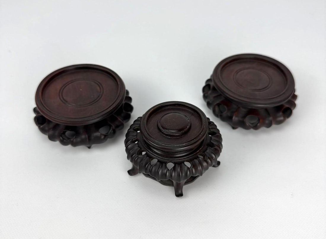 TRIO OF HAND CARVED HARD WOOD STANDS: Set of three dark-toned footed wooden pedestals with intricate openwork floral and scroll carvings for displaying porcelain or sculpture. Largest Approximate Dimensions: 4”Dia x 1.5” Artis