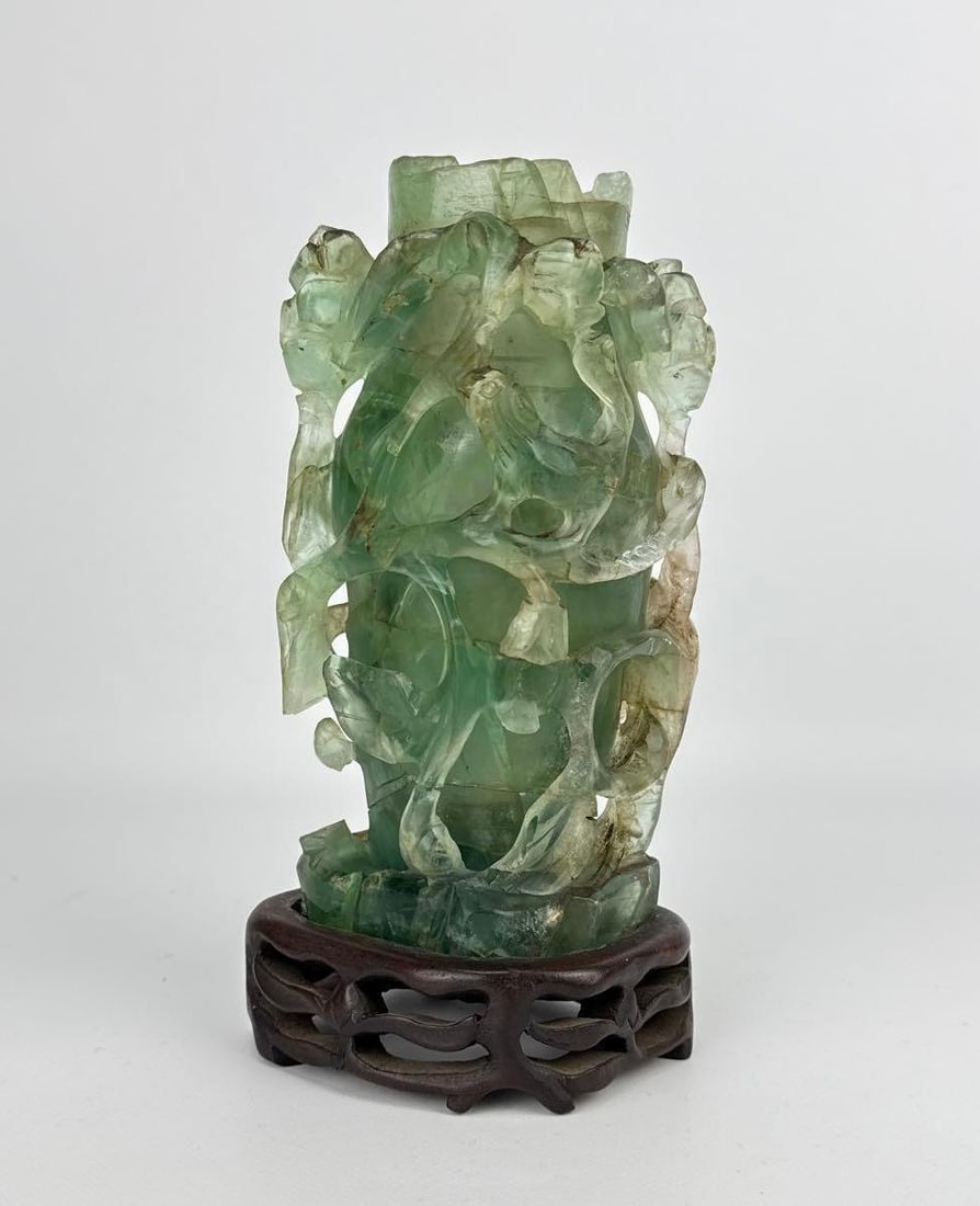 CHINESE HAND CARVED QUARTZ VESSEL ON WOODEN STAND: Translucent seafoam green hardstone vase intricately carved with high-relief climbing foliage and openwork branches. Cracks and losses throughout as pictured. Approximate Dimensions: 7.75”h x 4&