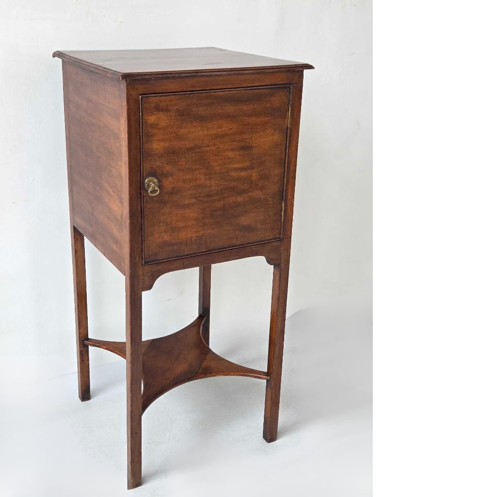 19TH CENTURY GEORGIAN MAHOGANY ONE DOOR CABINET: Slender 19th-century mahogany pedestal cupboard with a single flush-mount door, brass drop handle, and square tapered legs joined by an X-form stretcher. Approximate Dimensions: 32"h x 14.75"w