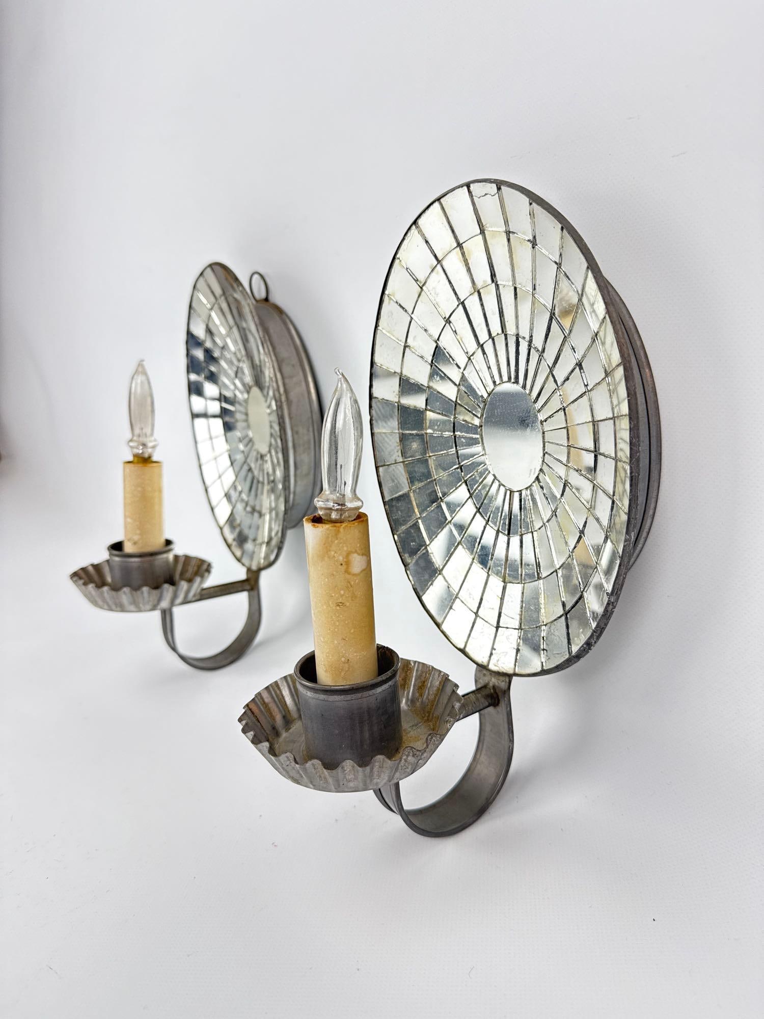 PAIR AMERICAN TIN MOSAIC MIRRORED ELECTRIFIED CANDLE SCONCES: Pair of handcrafted punched tin wall fixtures with arched tops and backplates composed of geometric mirrored glass tile mosaic. Approximate Dimensions: 9.75”h x 5.75”w x 5.5”d Artist