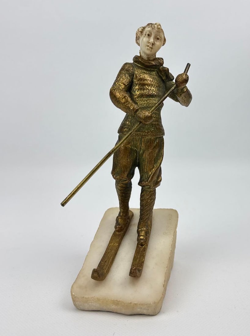 ANTIQUE GILTART DECO BRONZE SCULPTURE OF ALPINE SKIER UNSIGNED: A patinated and gilt art deco bronze figure of a man or boy in vintage winter attire on skis. Note: Missing bronze cap. Approximate Dimensions: 7”h x 2.75”w x 3.5”d Artist or Maker: 