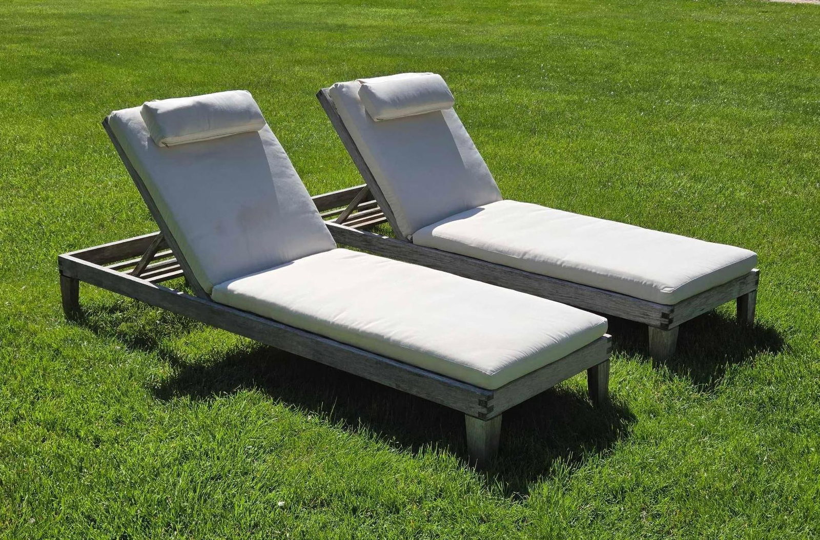 PAIR OF BARLOW TYRIE TEAK ADJUSTABLE BACK CHAISE LOUNGERS: Pair of professional grade weathered teak wood sun loungers with multi-position reclining backs and fitted cream cushions. Approximate Dimensions: 9"h x 78"w x 24.75"d; 30"h upright po