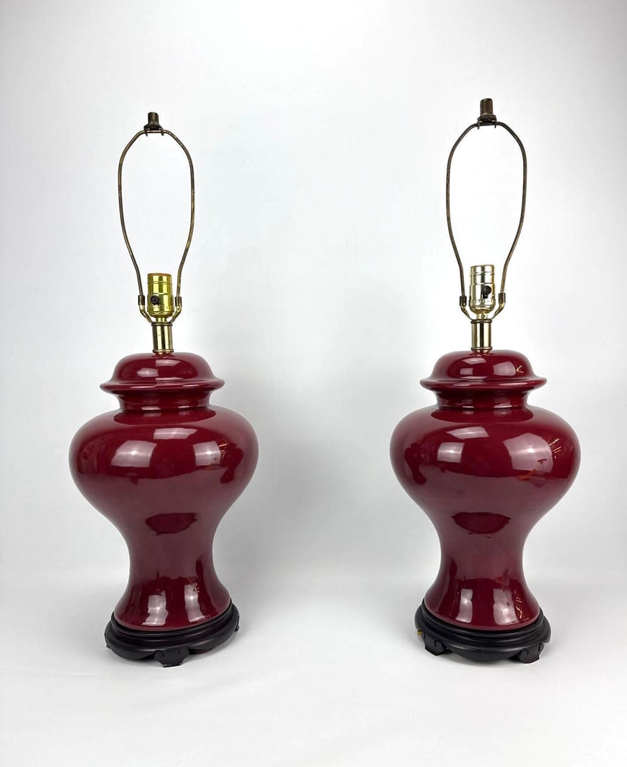 PAIR OF OXBLOOD PORCELAIN GINGER JAR STYLE TABLE LAMPS: Two deep red glazed ceramic ginger jar style lamps mounted on traditional dark wooden stands with brass hardware. Approximate Dimensions: 21”H x 10”Dia; Harp 28”H Artist or Maker: Un