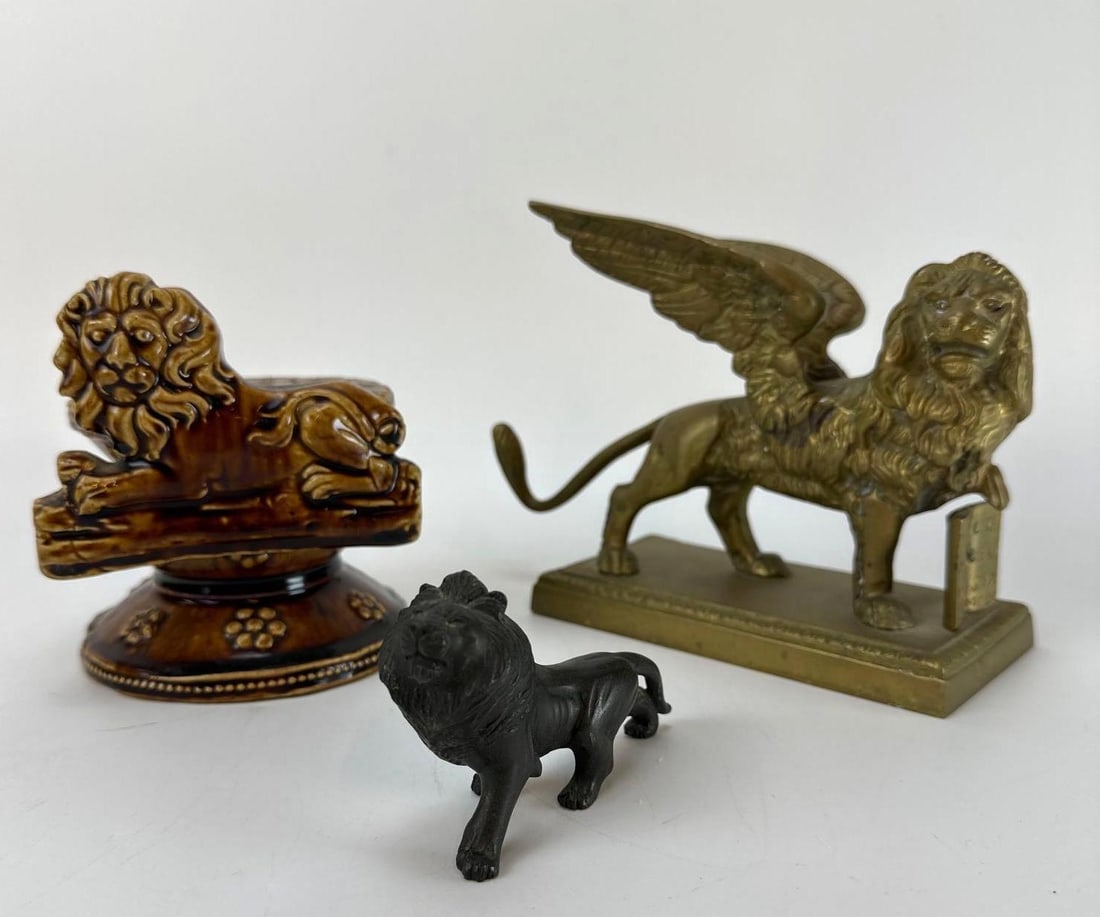 TRIO OF VINTAGE BRASS CERAMIC AND METAL LION FIGURINES: Three-piece eclectic shelf grouping consisting of a brass Lion of Saint Mark statue, a brown glazed pottery lion on a pedestal base, and a small black molded metal lion figure. Approximate Dimensions: