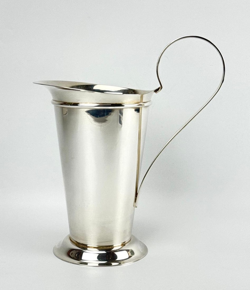 ROBERT A.M. STERN FOR SWID POWELL ITALIAN SILVERPLATED PITCHER: A sleek, silver-plated water pitcher designed by Robert A.M. Stern, with a tapered conical vessel on a flared circular foot with a dramatic loop handle. Approximate Dimensions: 11.25”H x 10&rdqu