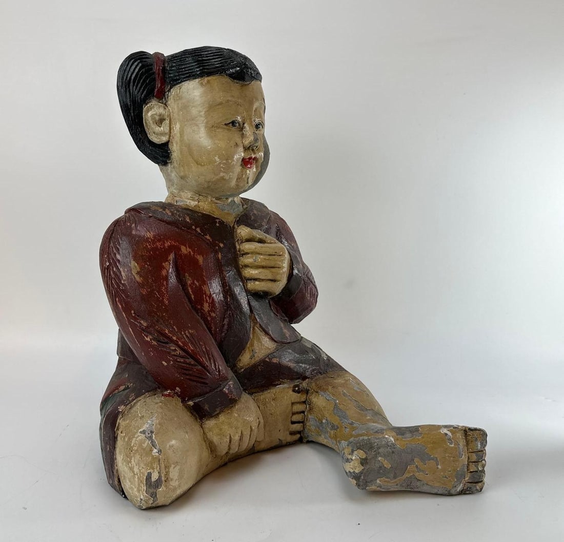 VINTAGE ASIAN HAND-CARVED PAINTED WOOD SEATED CHILD: A vintage folk art polychrome sculpture carved from solid wood depicting a seated child with molded pigtails, dressed in a traditional red-toned tunic. The piece features a heavily weathered, hand-pai