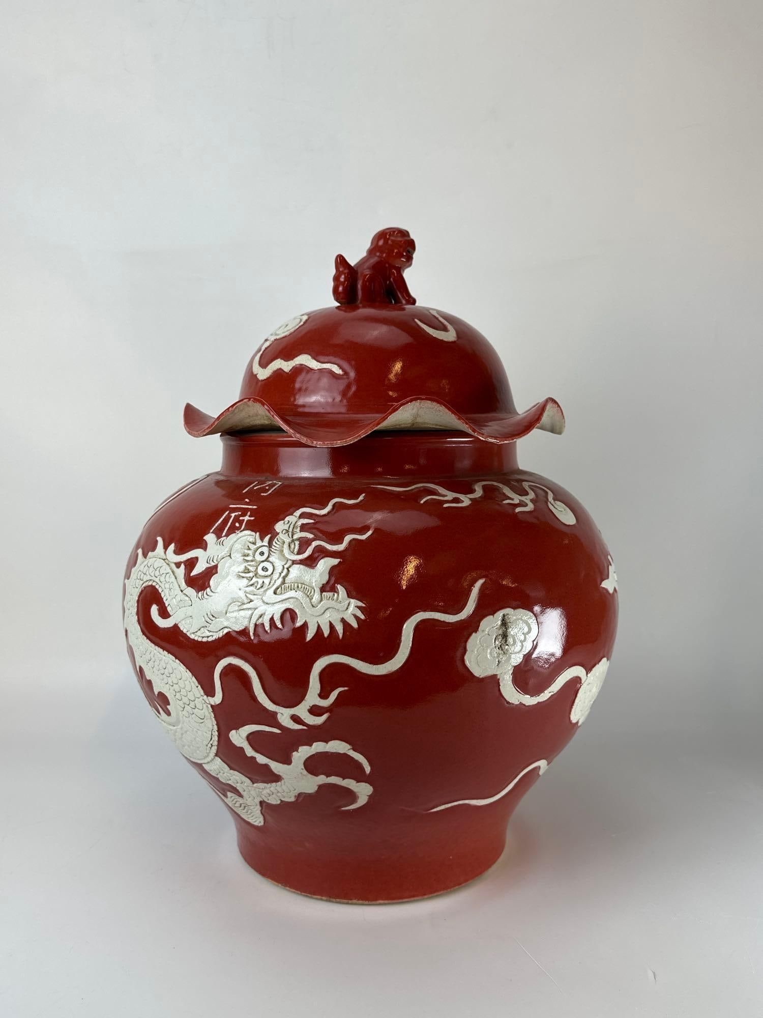 LARGE CHINESE SACRIFICIAL RED GLAZE PORCELAIN DRAGON TEMPLE JAR: *Lidded baluster-form ginger jar featuring a relief-decorated white slip dragon and clouds against a rich red ground with a foo dog finial. Approximate Dimensions: 18" tall x 13" dia Artist or