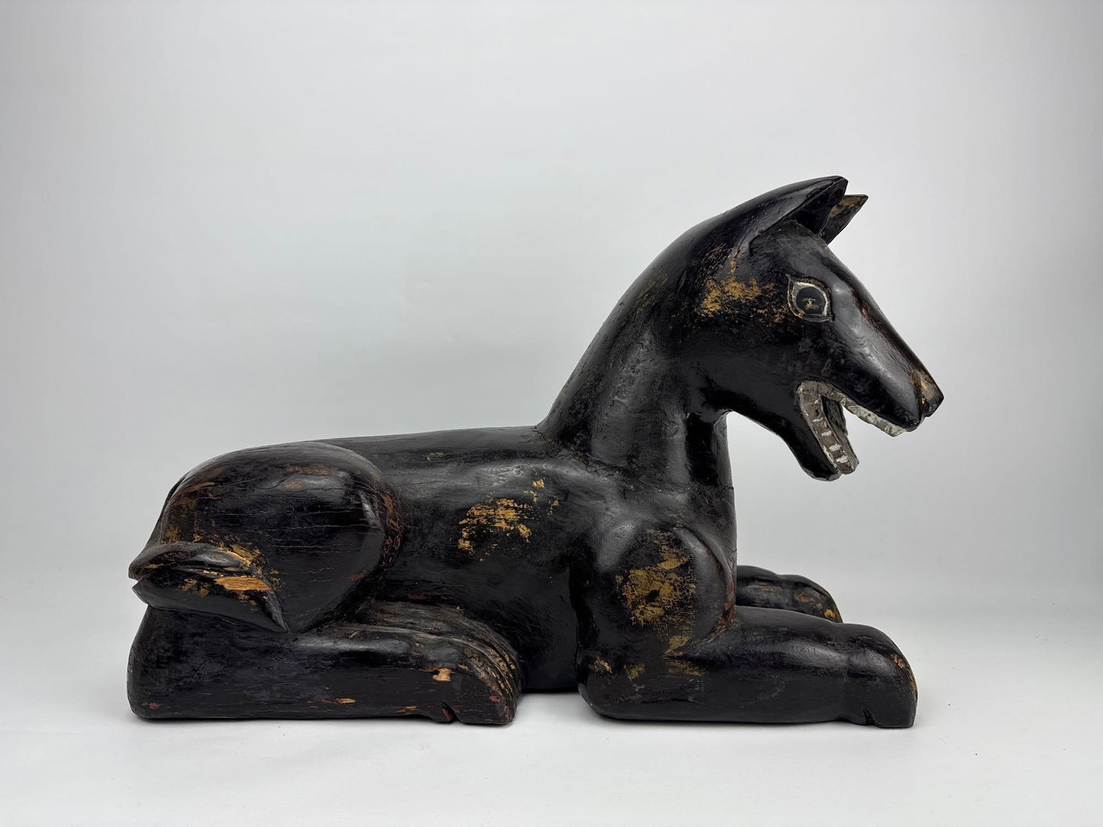 ANTIQUE ANUBIS/JACKAL; HAND CARVED BLACK LACQUER AND GILT WOODEN RECUMBENT GUARDIAN DOG: Large hand-carved folk art wooden sculpture depicting a resting mythical temple dog or protective guardian hound. Approximate Dimensions: 13.25”h x 8”w x 19.5”d Artist or Maker: Unkn