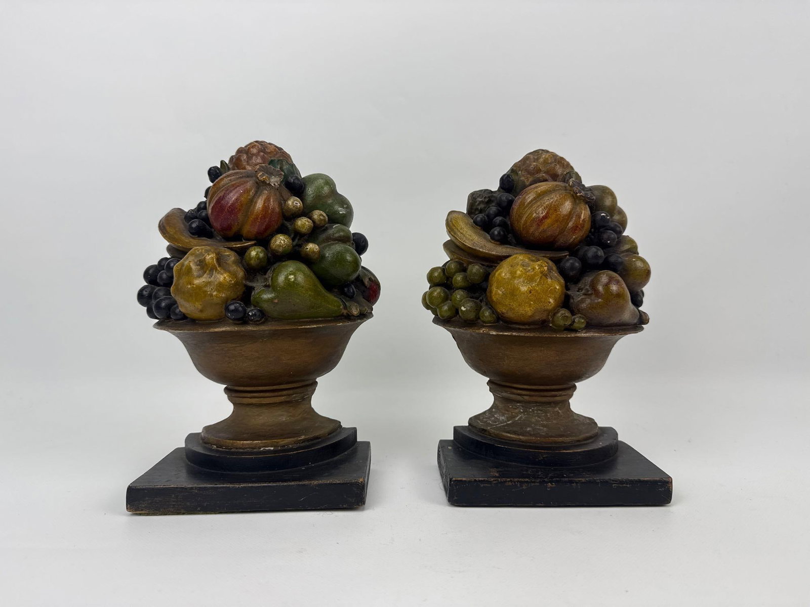 ANTIQUE FRUIT BOWL BOOK ENDS ON WOODEN BASE: Pair of bookends designed as footed compote bowls overflowing with an assortment of colorful harvested fruits mounted on square ebonized wooden bases Approximate Dimensions: 8.5”h x 5”w x 