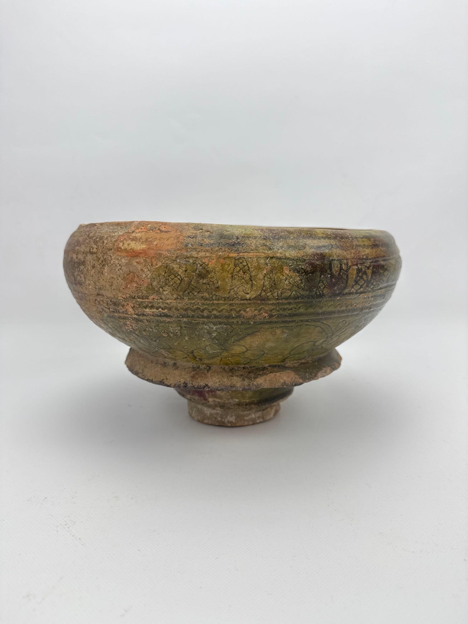 MIDDLE BYZANTINE SGRAFFITO CERAMIC FOOTED BOWL: Gazed pottery vessel from the 12th to 14th century AD adorned with incised linear and stylized floral motifs under a green and brown palette. Approximate Dimensions: 7”h x 11.5”round Artis