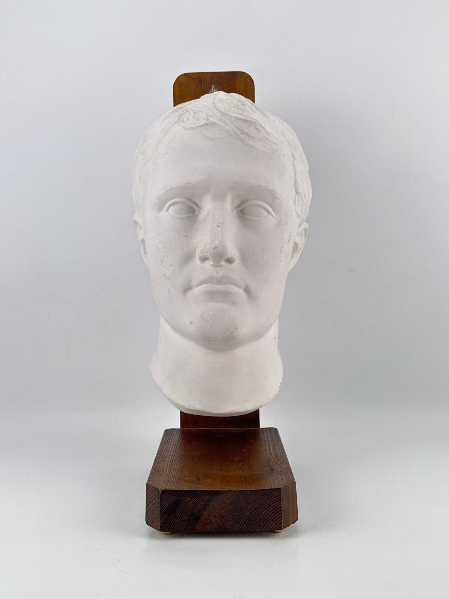 NAPOLEON AS MARS THE PEACEMAKER PLASTER BUST: A molded white plaster portrait head after Antonio Canova’s neoclassic sculpture of Napoleon Bonaparte, depicted with idealized Roman features and mounted to a custom dark wood display stand. Approx