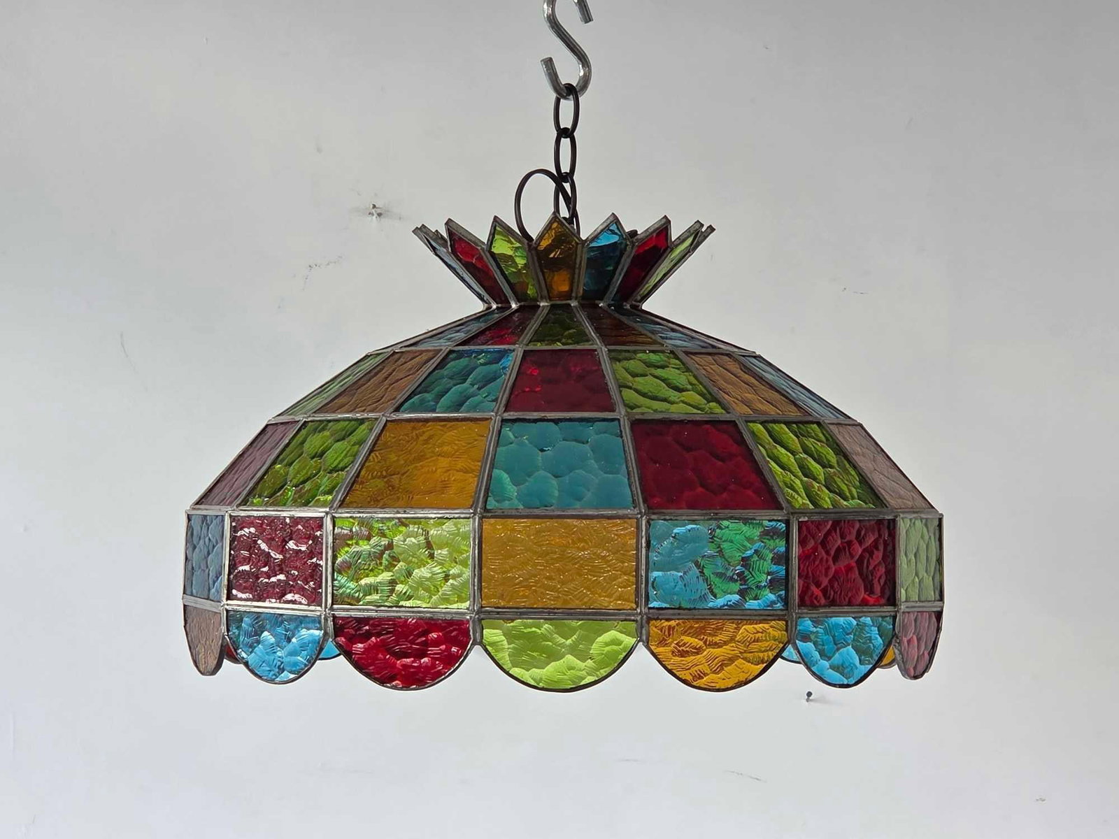 VINTAGE STAINED GLASS JEWEL TONED CHANDELIER: Suspended multi-colored leaded glass hanging light fixture composed of geometric textured slag glass panels arranged in a vibrant repeating pattern with a scalloped border. Approximate Dimensions:12&#