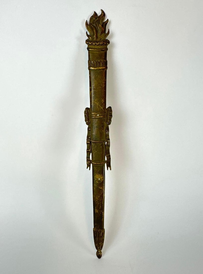 ANTIQUE GILT EMPIRE BRONZE TORCH WALL APPLIQUE: A long patinated gilt bronze wall hanging ornament shaped as a flaming torch with fluted body and ribbon bow accents in French Empire style. Approximate Dimensions: 15” x 1” Artist or Make