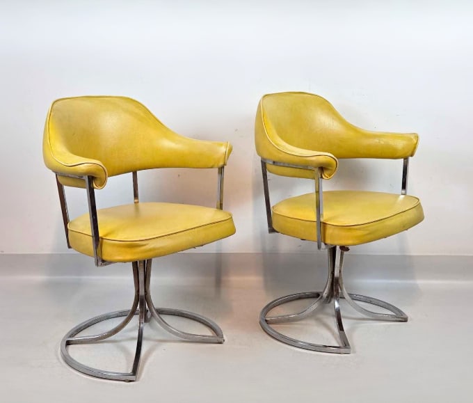 VINTAGE MID CENTURY CHROME AND YELLOW VINYL SWIVEL ARMCHAIRS: Pair of retro swivel armchairs upholstered in vibrant yellow faux leather on sculptural ribbon style chrome bases. Approximate Dimensions: 31"h x 24"w x 20"d Artist or Maker: Unknown