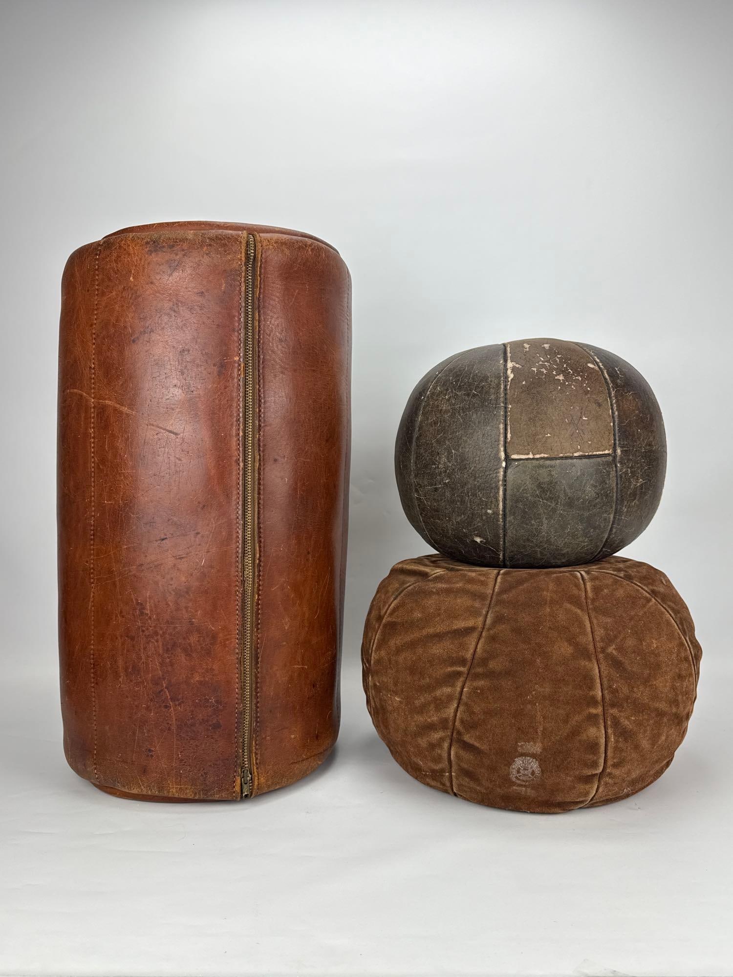 VINTAGE EVERLAST MANNER LEATHER MEDICINE BALLS & PUNCHING BAG TRIO: A three-piece collection of vintage athletic gym equipment consisting of two laced stitched leather medicine workout balls alongside one cylindrical brown leather punching heavy bag showing natural ag