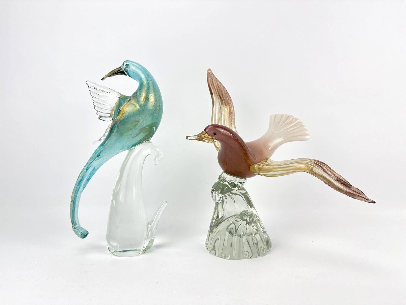 PAIR OF VINTAGE MURANO GOLD AVVENTURINA GLASS BIRD FIGURINES: Two mid-century hand-blown Italian art glass bird sculptures including a blue-green long-tailed bird on a clear perch and a multi-toned pink and amber bird with wings spread over a clear textured base
