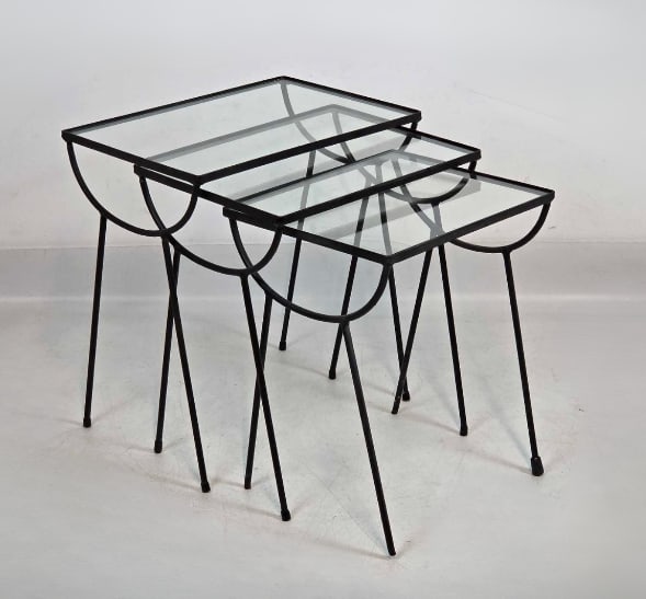 SET OF THREE MID-CENTURY MODERN BLACK WROUGHT IRON AND GLASS NESTING TABLES IN THE MANNER OF NELSON: Set of three graduating mid-century modern nesting side tables with clear inset glass tops resting on black-finished wrought iron frames with decorative semi-circular aprons and slender hairpin-style 