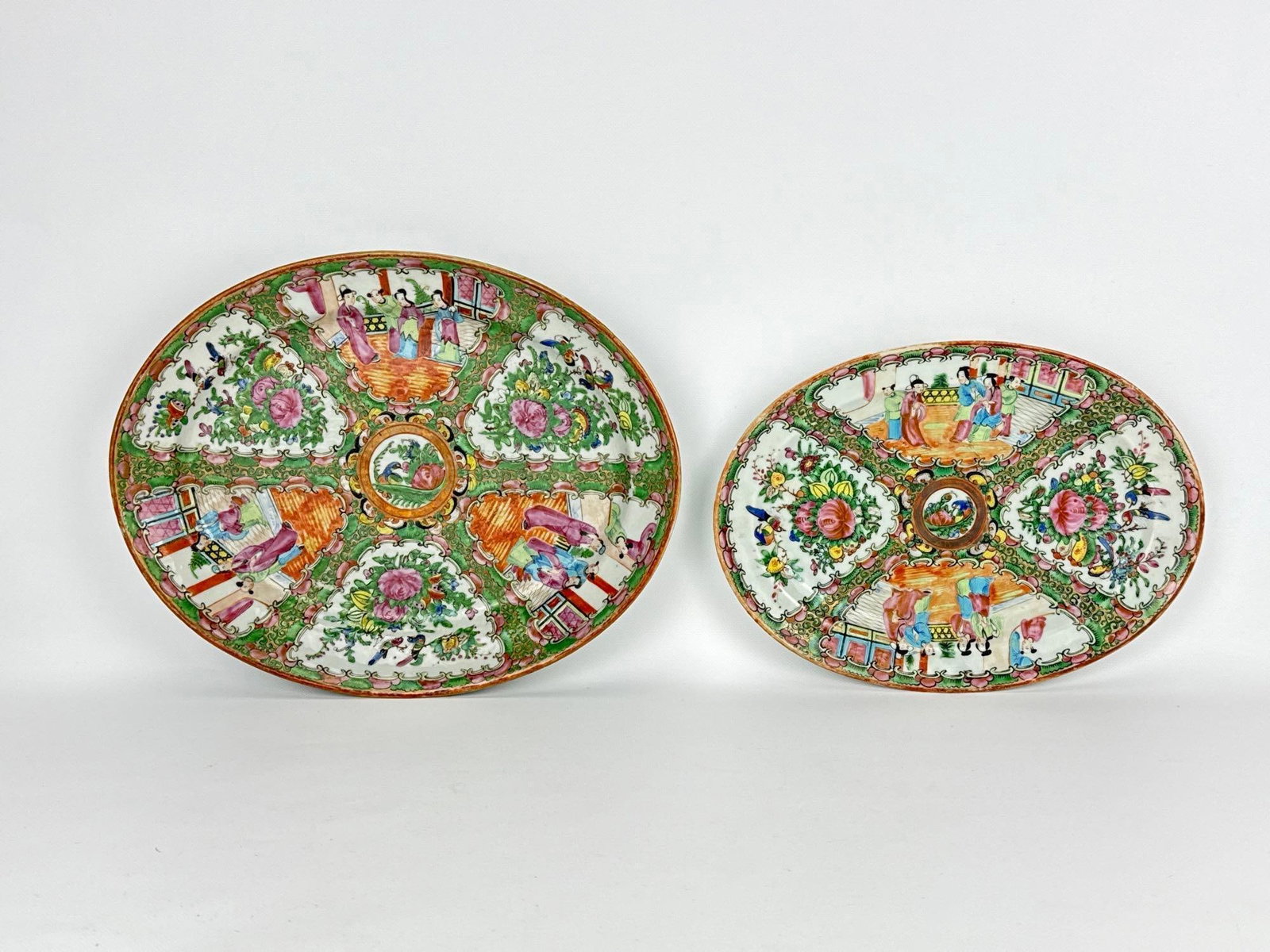 PAIR OF CHINESE EXPORT ROSE MEDALLION PORCELAIN OVAL PLATTERS: A graduated pair of early 20th-century Chinese export porcelain oval serving platters intricately decorated in the traditional Rose Medallion palette with alternating panels of courtyard figures and b