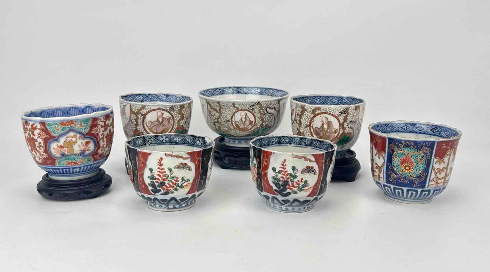 JAPANESE IMARI PORCELAIN SAKE AND TEA CUPS ASSEMBLED LOT OF 7: Assembled seven-piece collection of Japanese Imari hand-painted porcelain vessels comprising various tea cups and sake cups decorated with classical panels of figures, florals, and foliage, accompanie