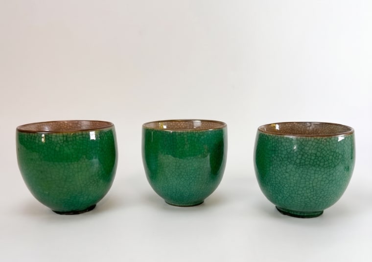 SET OF THREE CHINESE STYLE GREEN CRACKLE GLAZE CERAMIC TEA CUPS: Three Chinese style ceramic tea cups covered in a vibrant emerald green crackle glaze with a brownish-rimmed ge-type or guan-type style crackled interior. Approximate Dimensions: 3” h x 3.5&rdqu