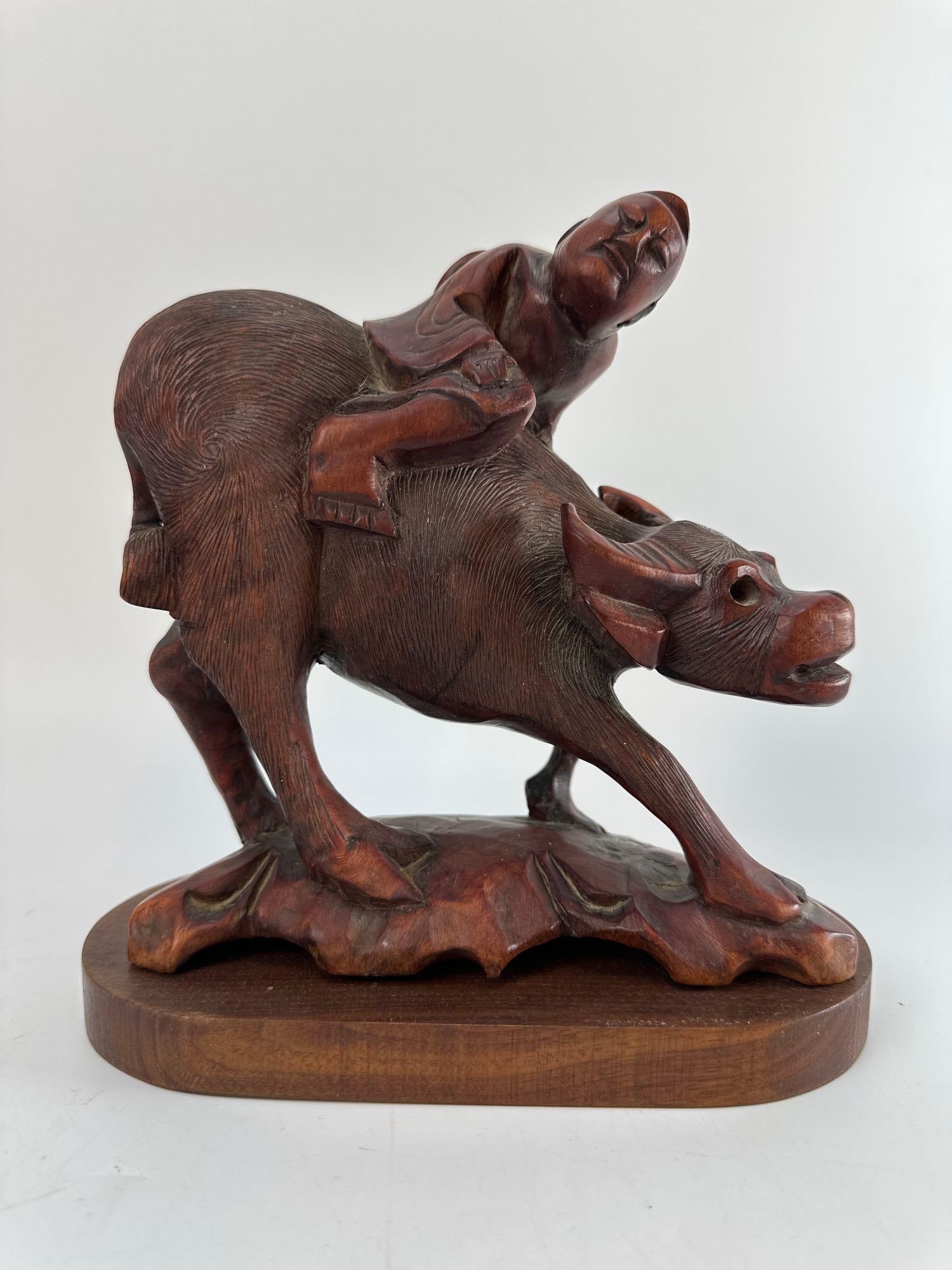 CHINESE CARVED HARDWOOD BOY RIDING WATER BUFFALO SCULPTURE: Hand-carved hardwood sculpture depicting a young boy clambering onto the back of a water buffalo on an integrated rockwork base, accompanied by a fitted wooden stand Approximate Dimensions: 9” H