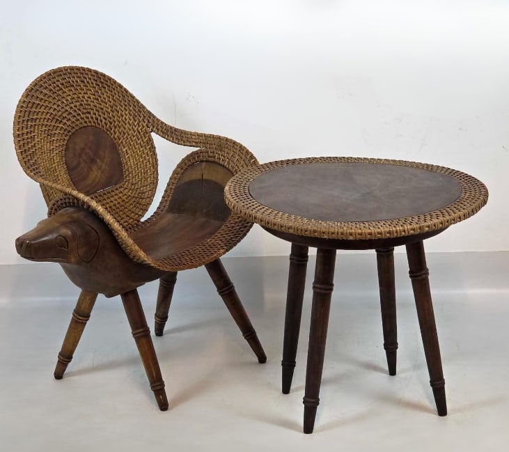 VINTAGE MIDCENTURY CARVED FOLK ART ZOOMORPHIC DOG ANIMAL CHAIR AND RATTAN TRIM SIDE TABLE SET: Unique two-piece indinesian 1960's vintage folk art furniture set comprising a primitive hand-carved monkey pod wood sculptural accent chair styled with an animal head and woven wicker fan backres