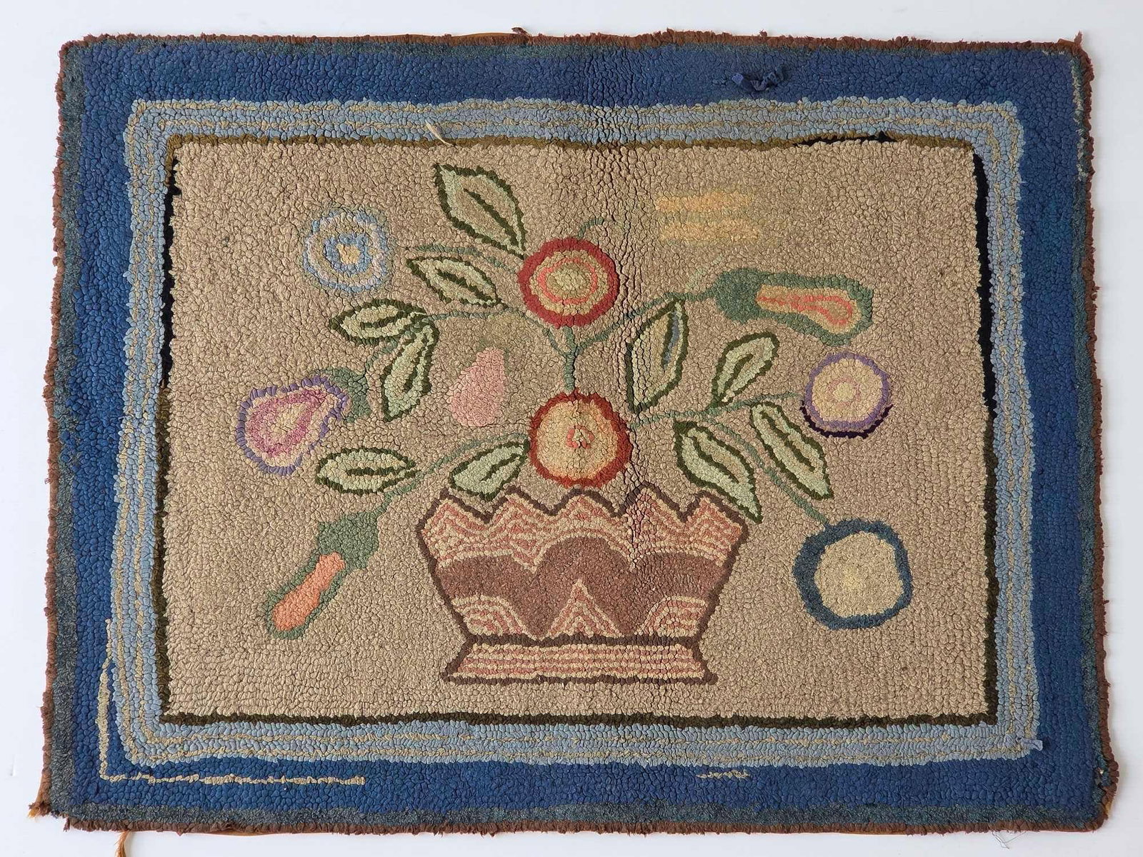 ANTIQUE AMERICAN FOLK ART FLOWER BASKET MOTIF HOOKED RUG: Antique American folk art hand-hooked pictorial rug depicting a stylized basket filled with multi-colored blossoms and trailing leaves within a layered blue border. Approximate Dimensions: 26.75" 
