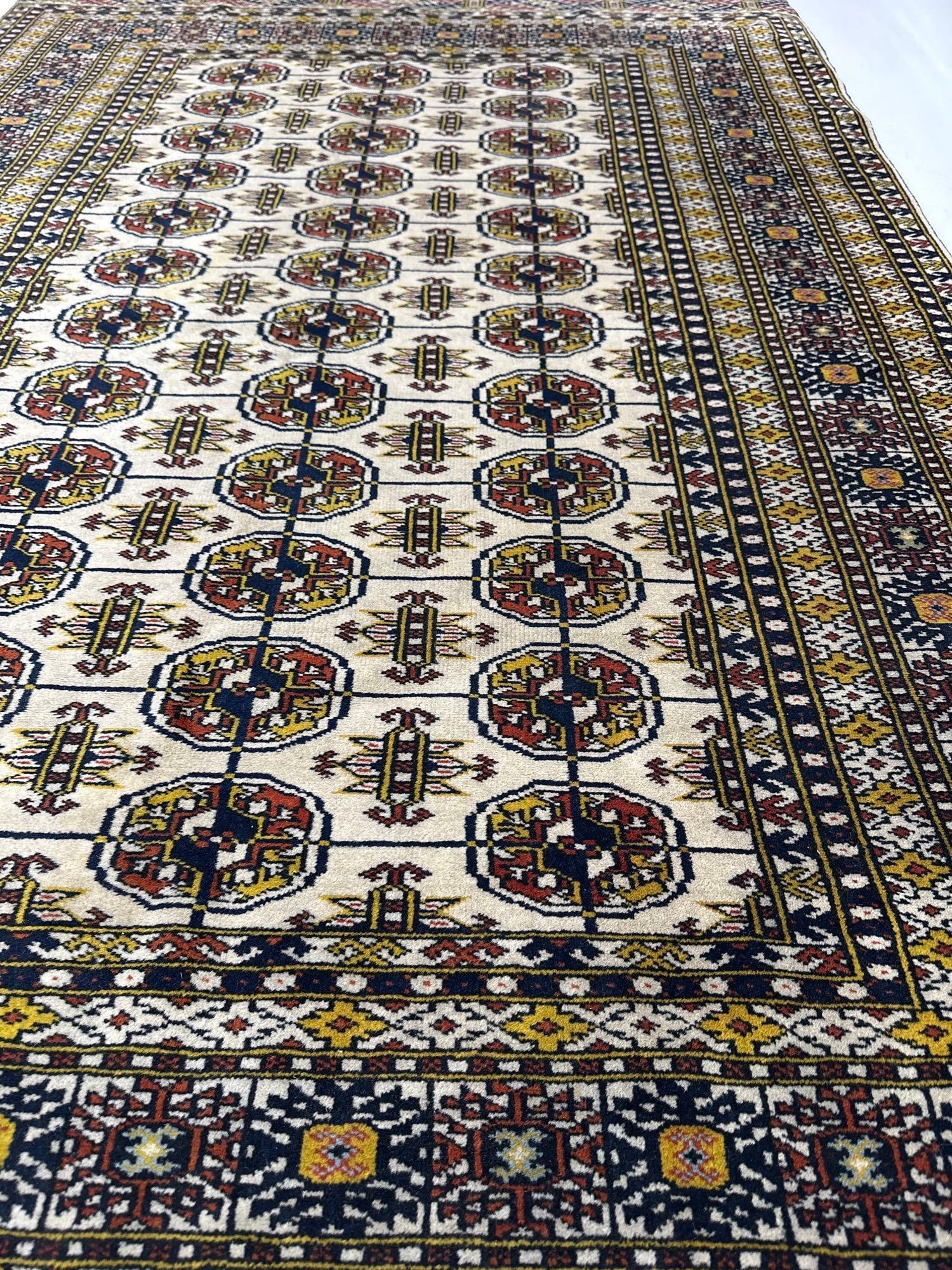TURKMEN BOKHARA HAND WOVEN ORIENTAL RUG: Hand-woven wool Oriental area rug with an ivory and cream field accented by repeating geometric Tekke gul motifs and intricate tribal borders. Approximate Dimensions: 50” x75” Artist or Ma