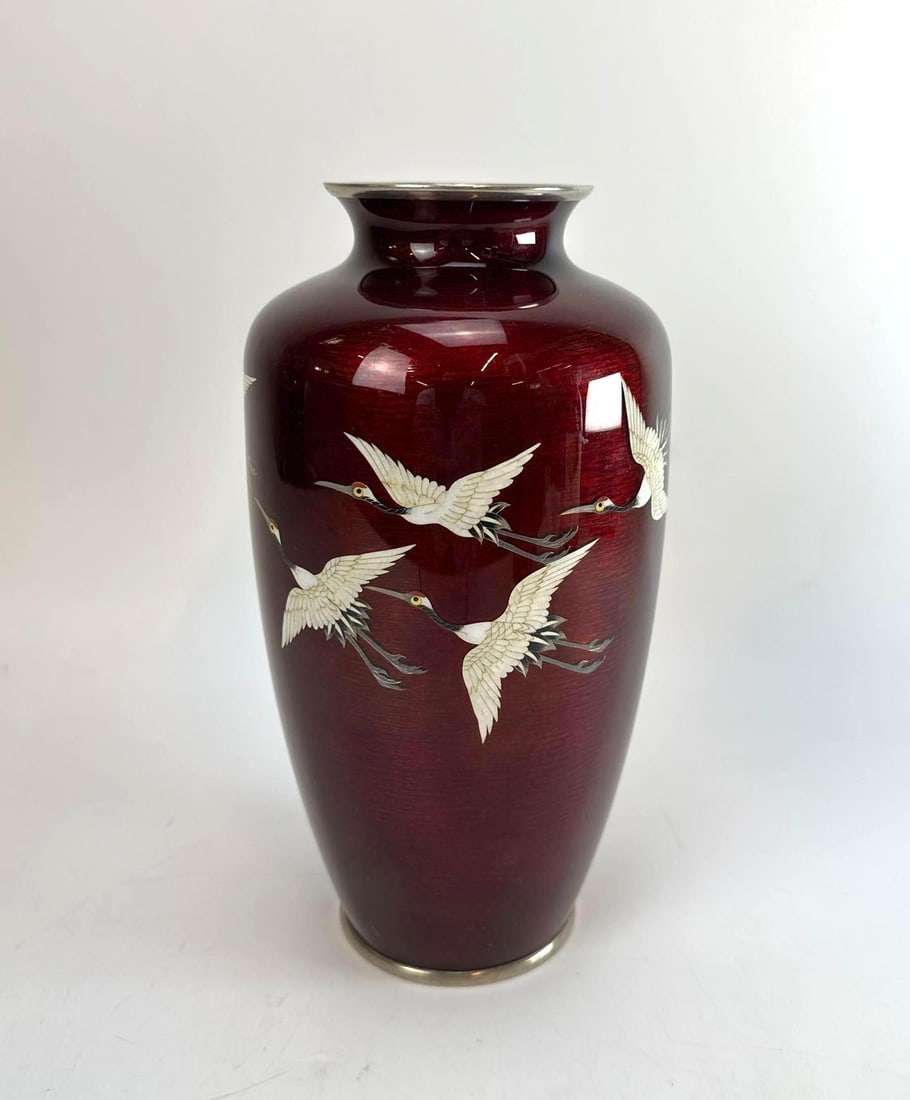 ANDO JUBEI JAPANESE PIGEON BLOOD GINBARI CLOISONNE FLYING CRANES VASE: A vintage hand-crafted Akasuke ruby red enamel-over-foil baluster vessel depicting detailed white cranes in mid-flight with silver-toned metal rims. Approximate Dimensions: 10"H x 6"Dia Artist