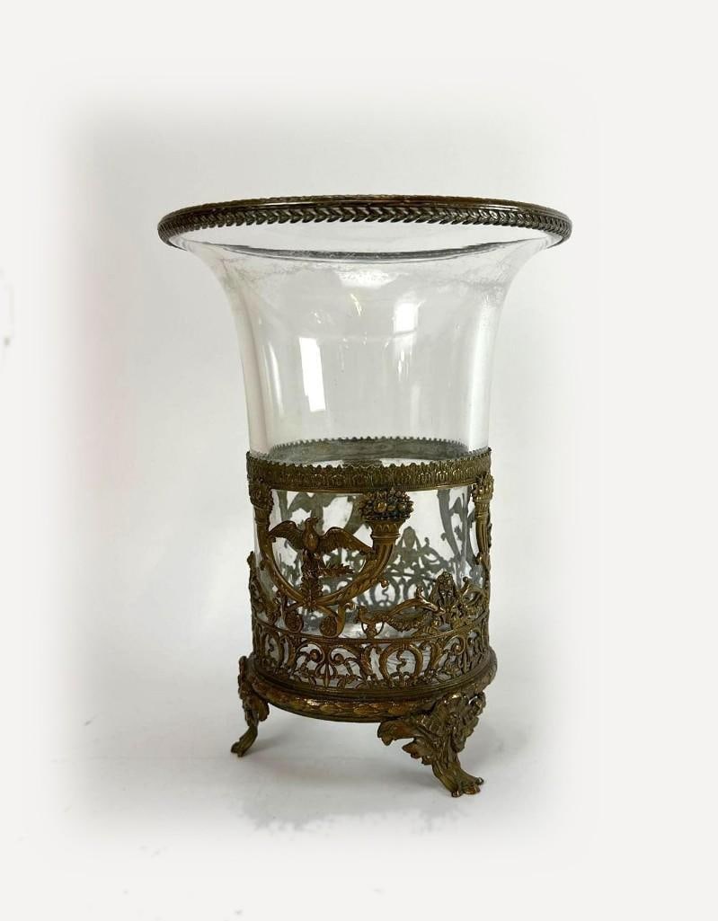 ANTIQUE FRENCH EMPIRE STYLE BRONZE DORE AND GLASS HURRICANE VASE: A 19th century style neoclassical flared clear glass vase set within an ornate, reticulated gilt brass footed base holder decorated with laurel swags and eagle motifs. Approximate Dimensions: 7”