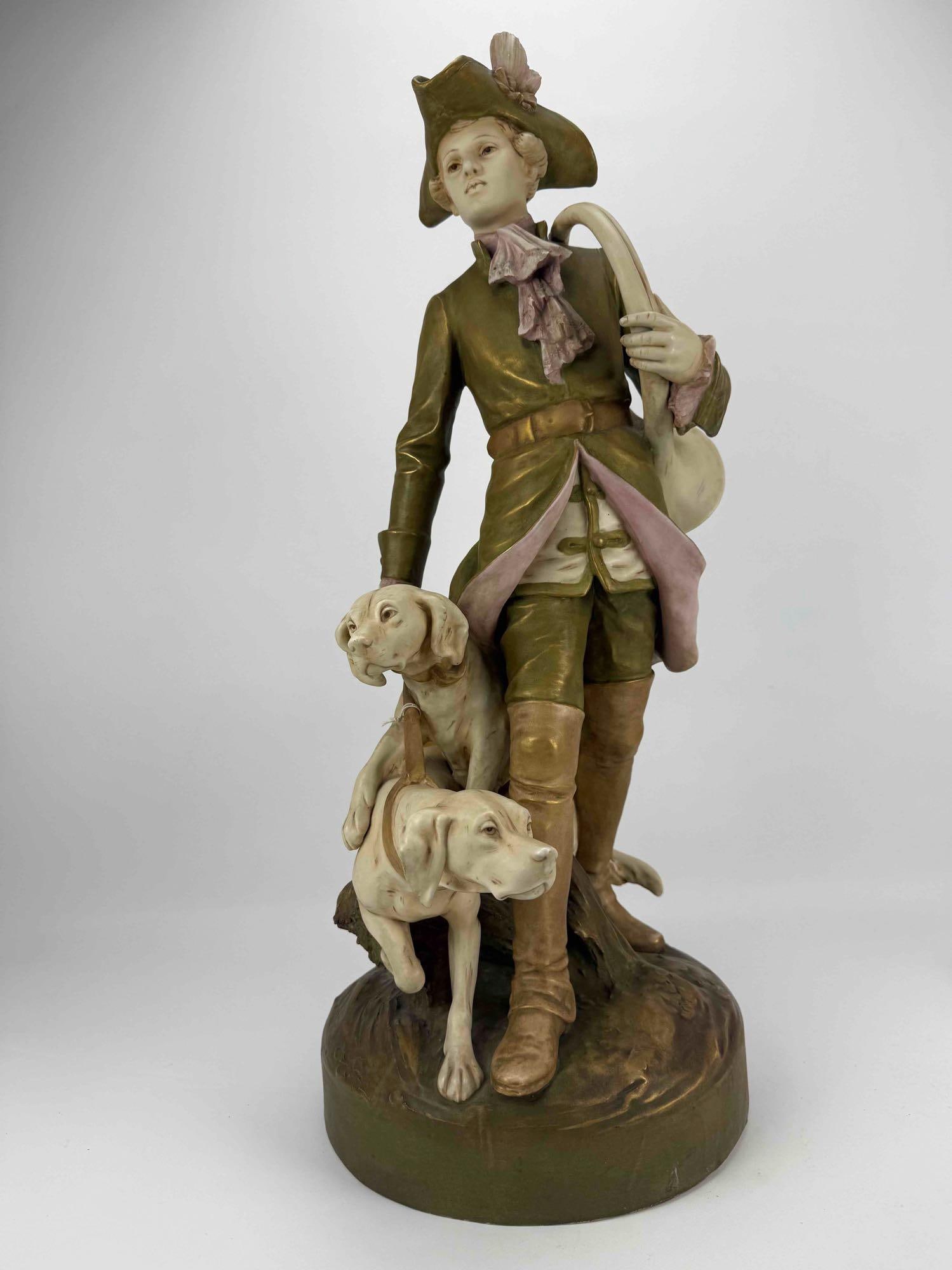 ROYAL DUX BOHEMIA "PIQUEUR AU RELAIS" PORCELAIN FIGURAL GROUP: *Large polychrome porcelain sculpture of a huntsman with two hunting hounds. Approximate Dimensions: 27.5”h x 13.5”d 11”dia at base Artist or Maker: Unknown Provenan